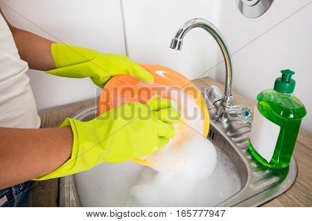 Close-up Of Person Washing Plate On Soapy Water In The Kitchen