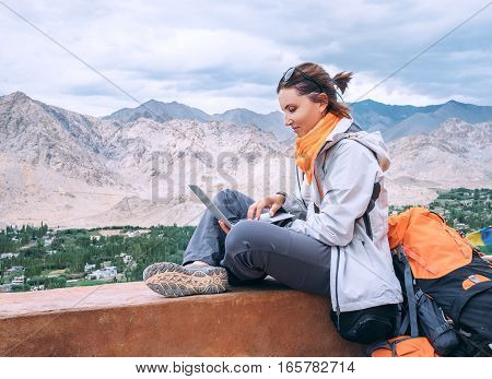 Backpacker with laptop sits on the top view point under mountain settelment