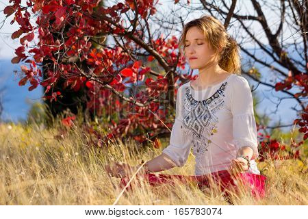 Young girl in a white shirt and red pants doing yoga outdoors