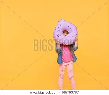 girl looking through a big violet donut over yellow background. Little kid holding a number zero with copy space. Null numeral