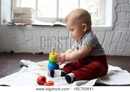 Сhild plays with a wooden pyramid on the floor
