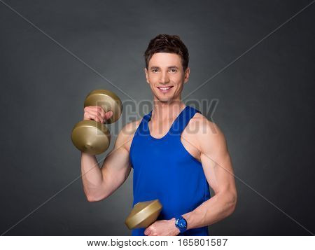 Handsome power athletic man in training pumping up muscles with dumbbells in a gym. blue t-shirt