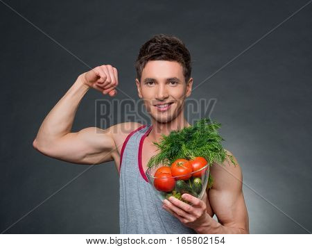 Young fittness trainer and nutritionist holding a bowl of vegetables, on black background