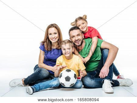 Happy family in colored t-shirts sitting together with soccer ball on white