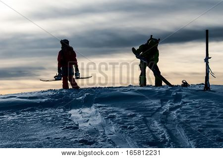 Silhouettes of two snowboarders on the mountain top before riding down in evening light