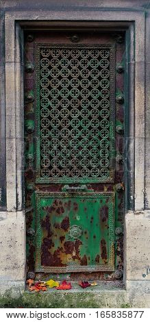 Rusty and shattered old green metal door. The iron is decaying and rusting. In the center is a repetitive pattern with small clover (quatrefoil) ornaments.