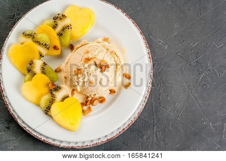 Romantic foods for Valentine's Day. Fruit salad with ice cream ball on a plate top view. Fruits cut in the shape of hearts