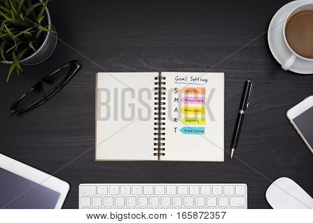 Smart goal setting on notebook with office supplies computer eye glasses and coffee cup over black table desk background view from above Business success concept