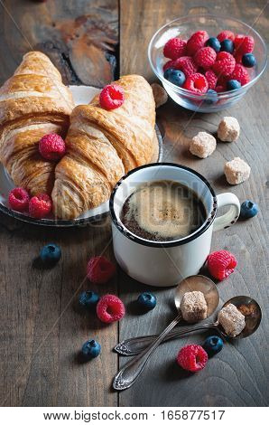 Coffee and croissants with raspberries and fruits for breakfast. Enamel mug. Toned image selective focus