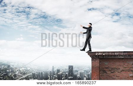 Businessman with blindfolder on eyes walking on building top