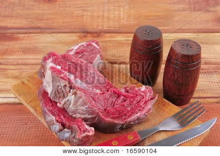 savory: bloody beef fillet (red meat) on wood with cutlery and castor