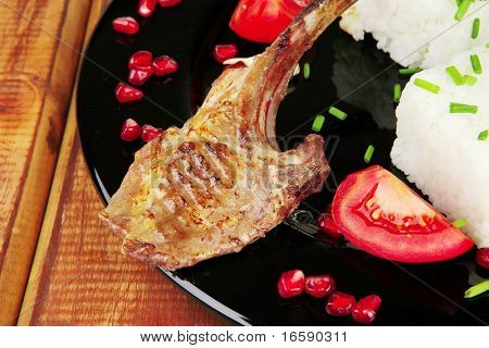 alimento della carne: costine su nero con contorno di riso e pomodori su nero su legno