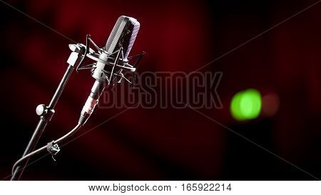 Shallow focus on a stand mounted condenser microphone with a green recording light showing in the background blur.