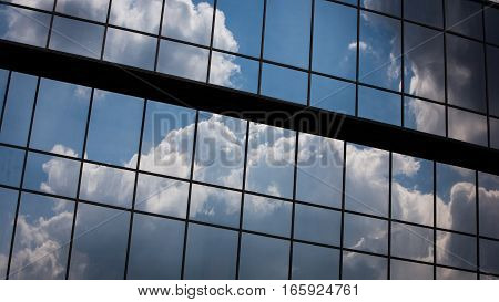 Abstract full frame office windows of an anonymous city skyscraper reflecting the blue sky and clouds.