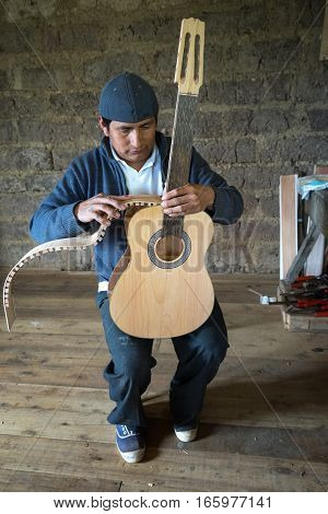 July 22 2016 San Bartolome Ecuador: an indigenous luthier holds up an unfinished guitar in his small rural shop