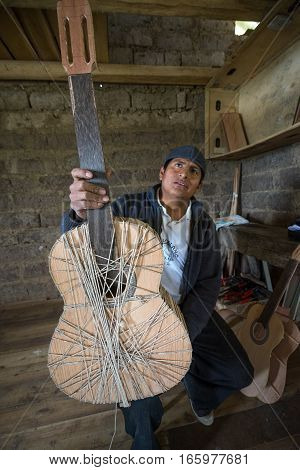 July 22 2016 San Bartolome Ecuador: an indigenous luthier holds up an unfinished guitar in his small rural shop