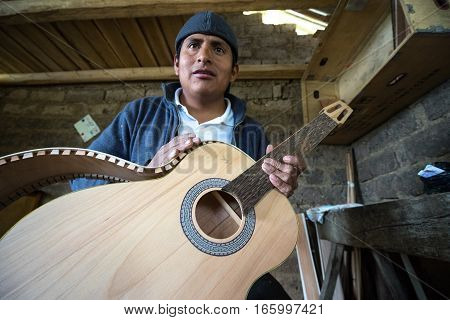 July 22, 2016 San Bartolome, Ecuador: an indigenous luthier holds up an unfinished guitar in his small rural shop