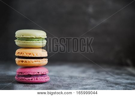 Stack of colorful assorted french macaroons on a dark stone background. Copy space for text. Wallpaper for fashion blogger. Horizontal