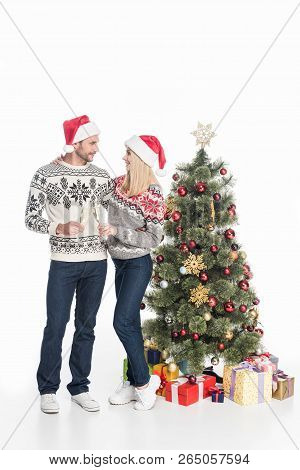 Couple In Love With Glasses Of Champagne Standing Near Decorated Christmas Treeisolated On White