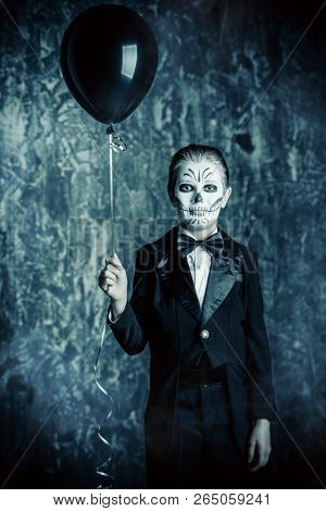 Portrait of a child boy with carnival make-up of a skeleton wearing elegant tail-coat. Studio shot over dark grunge background. Halloween. Dia de los muertos. The Day of the Dead.
