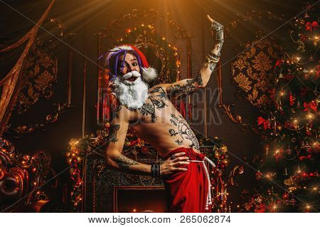 Bad Santa concept. Portrait of a nude tattooed Santa with purple dreads demonstrating antisocial behavior, rudeness and aggression. 