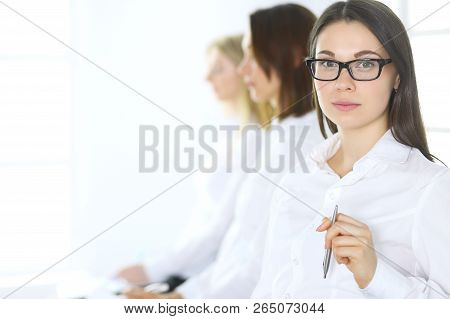 Attractive Businesswoman At Meeting Or Conference Against The Background Of Colleagues. Group Of Bus