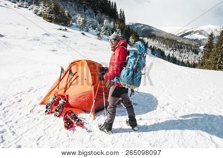 Camping In The Snow. Winter Trekking In The Mountains. Orange Tent, Snowshoes And Trekking Poles. A 
