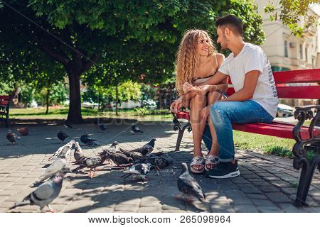 Young Mixed Race Couple In Love Feeding Bidrs In Summer Park. Man And Woman Thowing Bread To Doves