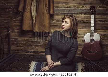 Vintage Portrait Of Beautiful Stylish Girl With Turquoise Earrings In Old Wooden Hut With Guitar And