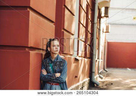 Proud Little Girl In Jeans Clothes Stands Near An Old Restored Beautiful Building.
