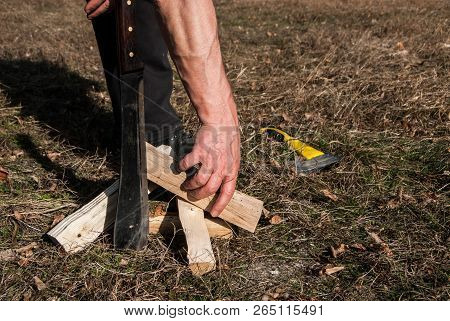 Strong Man Hand Takes Firewood To Set Fire. Big Steel Knife Or Machete Is Put Into The Ground And Ax