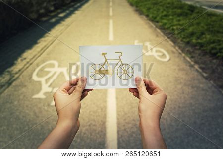 Close Up Of Woman Hands Holding A White Paper Sheet With Bicycle Icon Over Bike Lane Background. Hea
