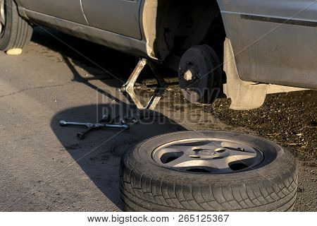 Replacing The Rear Wheel Of The Car. The Car Is Mounted On The Jack. On Asphalt Lie Screws, Tool And