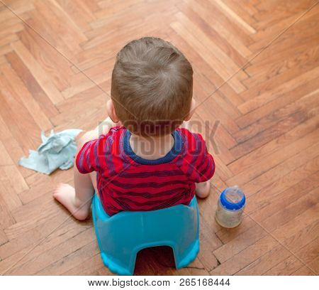 Little Baby Sitting On Chamber Pot With Toilet Paper And Pacifier On A Brown Background