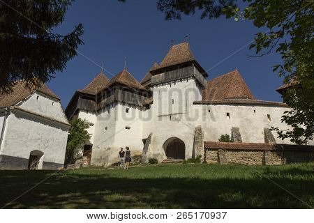 Viscri, Romania - April 29, 2018: Viscri Fortified Town Entrance In A Spring Day. Two Tourists In Fr