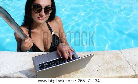Sexy Girl In A Black Bikini Uses A Laptop With A Black Screen In The Pool. Work On Vacation. Glamoro