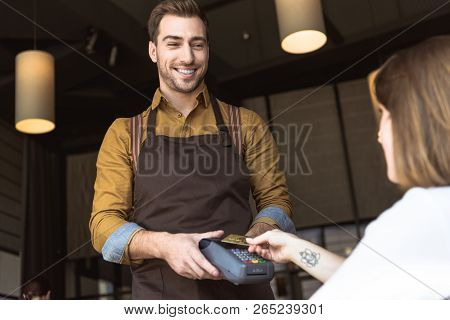 Smiling Young Waiter Holding Payment Terminal While Customer Doing Contactless Purchase With Credit 