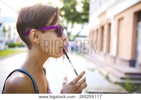 A Girl Drinks A Drink Through A Straw. A Woman In Glasses Drinks Morning Coffee On A City Street. A 