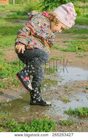 Little Girl In Boots Trampling A Muddy Puddle In Autumn