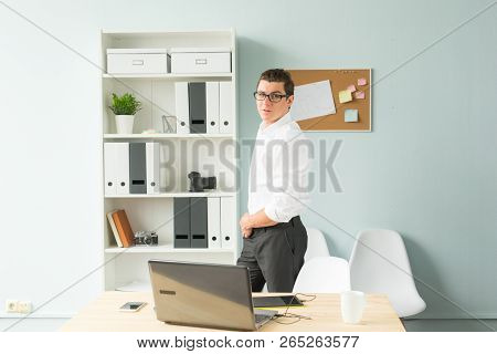 Business, Office, People Concept - Handsome Man In Glasses Stands In The Office Near A Computer And 