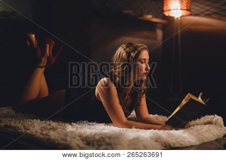 Glamour Woman With Long Brown Hair Lying In Black Sexy Body On A Carpet Under Bookshelf Reading A Bo