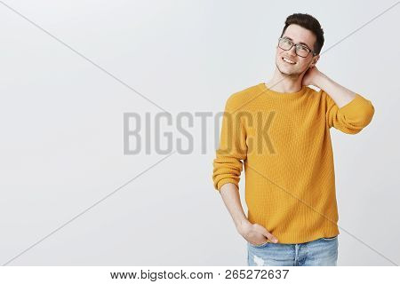 Indoor Shot Of Charming Nice And Handsome Young Guy In Glasses And Yellow Sweater Touching Back Of N
