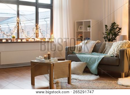 interior, christmas and interior concept - cushioned sofa, coffee table, garland string and candles on window sill in living room of cozy home