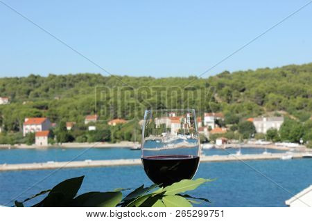 glass of wine and laurel branch with mediterranean village in background, island Zlarin, Croatia