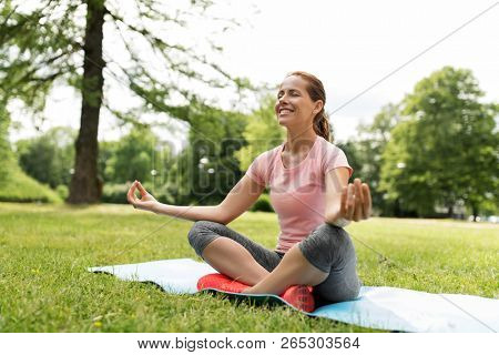 fitness, yoga and healthy lifestyle concept - happy woman meditating in summer park