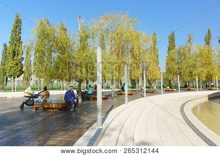 People Sit On Wooden Benches Under The Willows Near The Pond Of The New City Park Krasnodar Near The