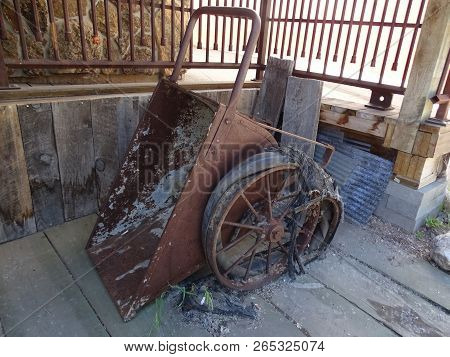 An Rusty Antique Industrial Tipping Wheelbarrow With Dilapidated  Wheels