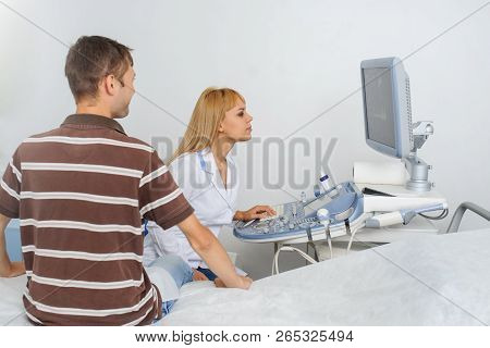 The Lady Ultrasunography Doctor Is Explaining To The Patientat Divice, In Medical Office