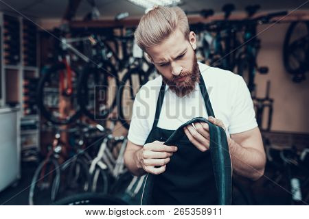 Young Mechanic Repairs Bicycle In Bike Workshop. Portrait Of Bearded Man Wearing White T-shirt And A