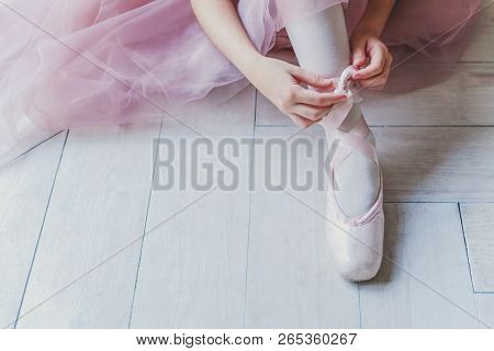 Hands Of Ballerina In Pink Tutu Skirt Puts On Pointe Shoes On Leg In White Light Hall. Young Classic